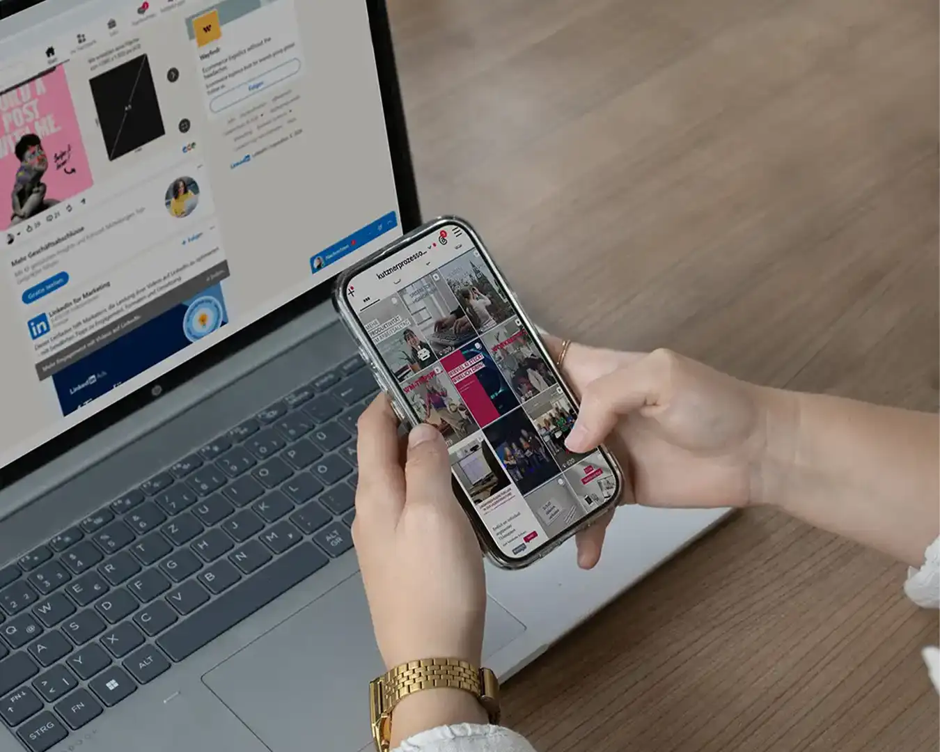 Eine Person sitzt an ihrem Laptop, auf dem LinkedIn geöffnet ist und stöbert auf ihrem Handy auf Instagram